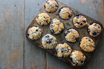 A dozen homemade blueberry muffins in pan on a rustic blue table, copy space, edge, vertical, angled, from above