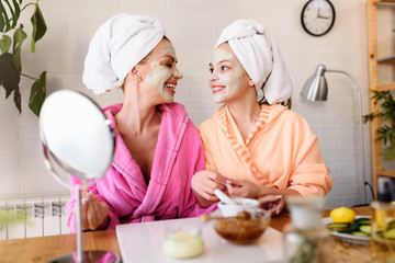 Mother and daughter in bathrobes and towels on head using natural cosmetics and having fun together...