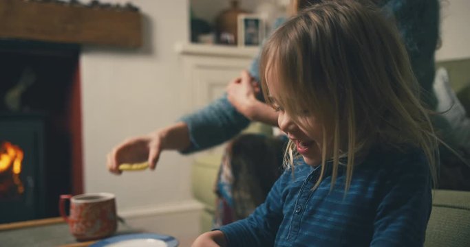 Young mother and toddler eating biscuits and drinking tea by fire