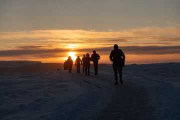 Fototapeta na wymiar Silhouette of group of tourists walking through snow at sunset in Iceland