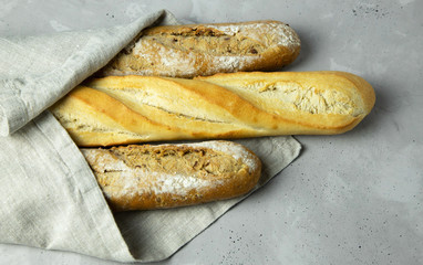 Three baguettes on a brown linen napkin lie on a gray concrete background. Bread. Bakery