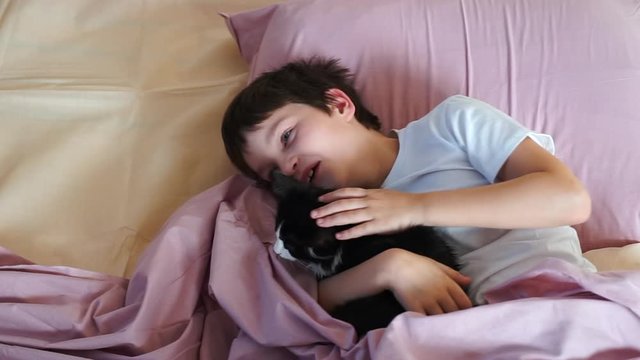 child boy sleeping together with a cat. close up. Cute child hugging, holding and petting kitten lying in bed. Fluffy black cat. Cozy morning at home. friendship and pet love.