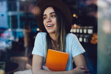 Exited female student with book sitting in cafe