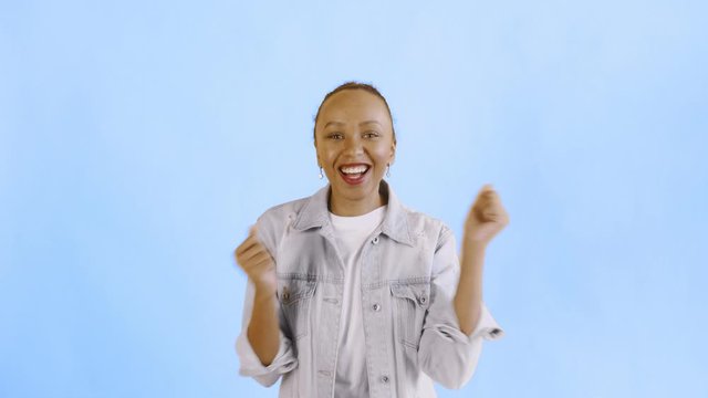 Beautiful happy african young woman saying OH MY GOD and dancing on blue background Jean jacket