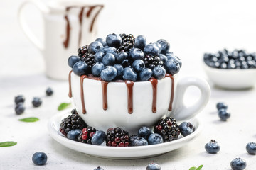 Chocolate mug cake with blueberries and blackberries in a white ceramic mug on white background