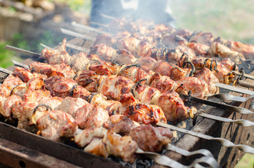 Meat with smoke on a barbecue grill over charcoal. Grilled cubes of meat on metal skewer. Meat on skewers is roasted on fire