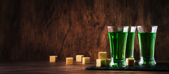 Absinthe - strong alcoholic drink, green bitter wormwood tincture in glasses on the old wooden...