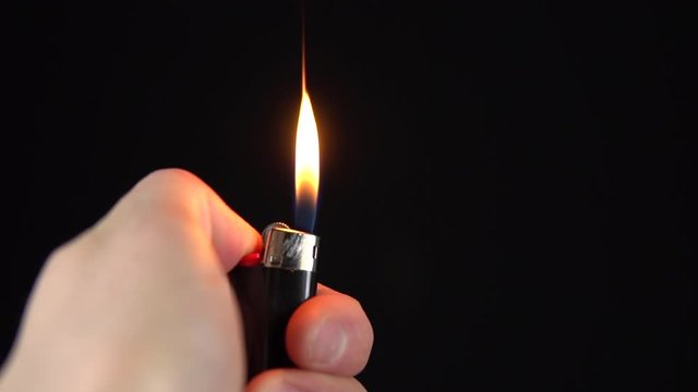 A man lights a lighter. A man holds a lighter in his hand and spins a drum on a black background. The lighter emits sparks and ignites closeup. Slow motion