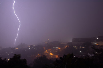 Naklejka na ściany i meble Heavy rainfall in the historic city centre of Ouro Preto in Brazil during a storm with lightning slicing through and illuminating the hazy night sky