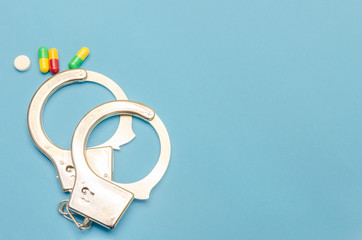Handcuffs and pills on a blue background with a copy of the space