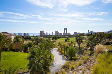 Fototapeta na wymiar Green golf course and skyscrapers on the horizon and blue sky with beautiful clouds in Benidorm, Spain