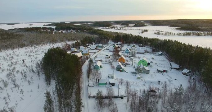 View from above at Russian village covered with snow, drone flyng in forest of Karelia at sunset in winter season