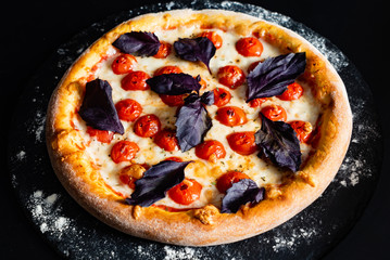 tasty pizza with cherry tomatoes on the black background