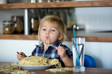 Little baby boy, toddler child, eating spaghetti for lunch and making feeding teddy bear friend