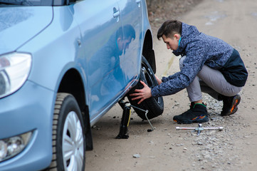 A man broke a wheel on a car and changes it on his own on the road.