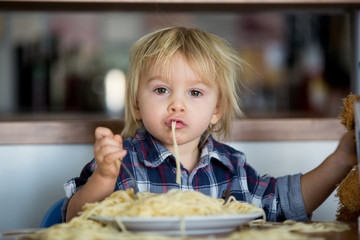 Little baby boy, toddler child, eating spaghetti for lunch and making feeding teddy bear friend