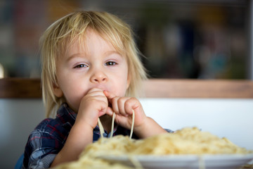 Little baby boy, toddler child, eating spaghetti for lunch and making feeding teddy bear friend