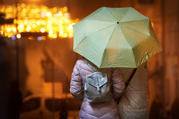 Couple of females with umbrella outdoors on rainy evening in the decorated street. Female holding an umbrella, explores the christmas decorated city center during night time with street lights