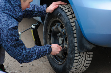 A man broke a wheel on a car and changes it on his own on the road.