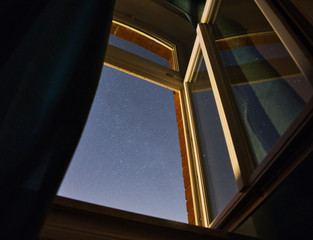 Langzeitbelichtung des Sternenhimmels durch ein geöffnetes Zimmerfenster