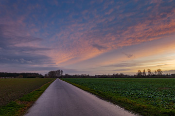 Beautiful dramatic orange and blue cloud and sky after storm and raining over agricultural field and road on countryside area in German. Nimbostratus cloud during sunset. 