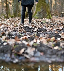 Frau auf Spaziergang im Herbst im Wald mit matschigem Boden und Laub