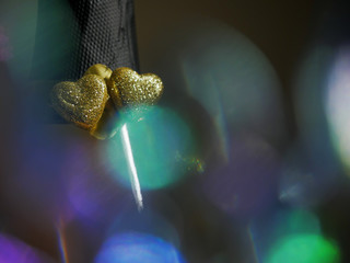 Tow golden hearts symbol of love on a neck of champagne bottle, abstract Saint Valentine background. Blurred colorful glass in foreground.