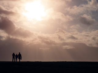 Silhouette of three people on a walk against beautiful warm cloudy sky with sun rays and flare.