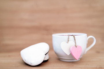 Heart shaped tea bag in white cup of tea with ginger cookies - cute love declaration on wooden background, selective focus. Valentines day concept. Mug of tea for two lovers honeymoon wedding morning