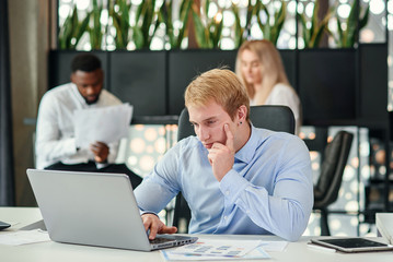 Obraz premium Enterprising caucasian office manager sitting at his workplace at office and studying report's datas in the meeting room.