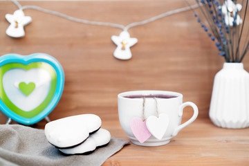 Heart shaped tea bag in white cup of tea with ginger coocies - cute love declaration on wooden background, selective focus. Valentines day concept. Mug of tea for two lovers honeymoon wedding morning