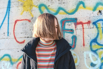 Beautiful teenage girl with short hair posing near graffiti wall. Urban outdoors, teenager's lifestyle