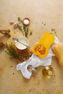 Halved butternut squash with cream, thyme and garlic on beige background. Ingredients for cooking dinner. Flatlay.