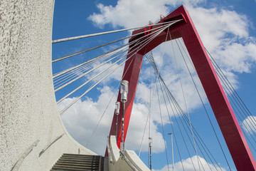 Red metal bridge, with suspension cables in Rotterdam, Holland, Netherlands. Sunny day with clouds.