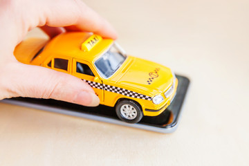 Smartphone application of taxi service for online searching calling and booking cab concept. Hand holding yellow toy car Taxi Cab on empty screen of smart phone on wooden background. Taxi symbol.