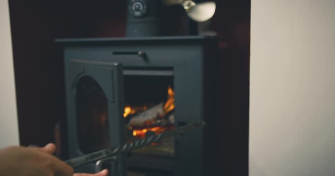 Young mother stoking fire in logburner with her toddler in her lap