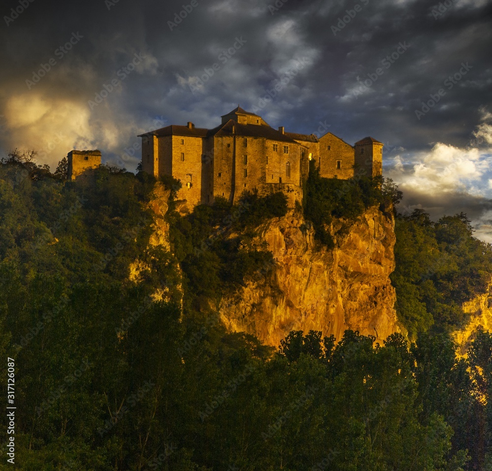 Sticker Chateau de Bruniquel surrounded by greenery and rocks under a cloudy sky during sunset in France