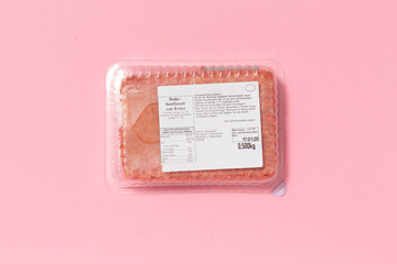 Black plastic pack with fresh hash isolated on pink background. Raw meat packed with label top view, Symbol for environmental pollution done by the food industry