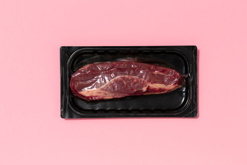 Black plastic pack with fresh beef steak isolated on pink background. Raw meat packed without label...