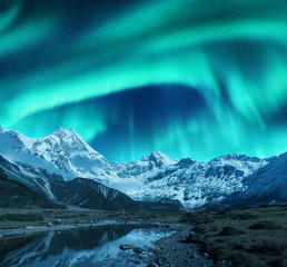 Aurora borealis over the snowy mountains, coast of the lake and reflection in water. Northern...