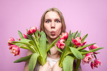 beautiful girl holding a bouquet of flowers on a pink background, happy woman with tulips surprised