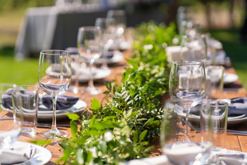 Beautifully decorated wooden table in a summer open-air cafe. Green branch and fresh flowers table decoration