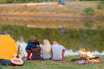 A group of friends is enjoying view, camping with bonfire on riverside