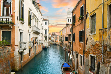 Fototapeta na wymiar A colorful sky matches the colors of the medieval walls and canal in the historic center of Venice, Italy.