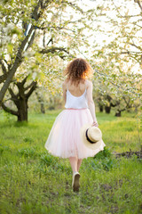 Young attractive woman with curly hair walking in a green flowered garden. Spring mood