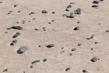 Fototapeta na wymiar Small stones and pebbles are scattered on the brown-yellow sand