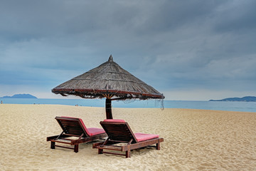 Straw parasol with two loungers at the tropical beach 