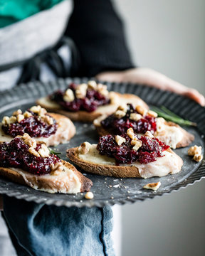 A woman holding a tray of cheese crostini with rosemary cranberry fig jam