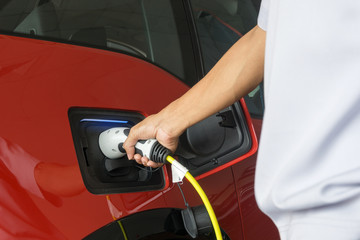 Hand of man holding connecting plug for charge electric power into Battery of Electric car on...