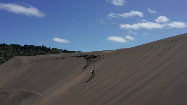 Woman walking up high sand dunes along Bethells Beach, Auckland, NZ